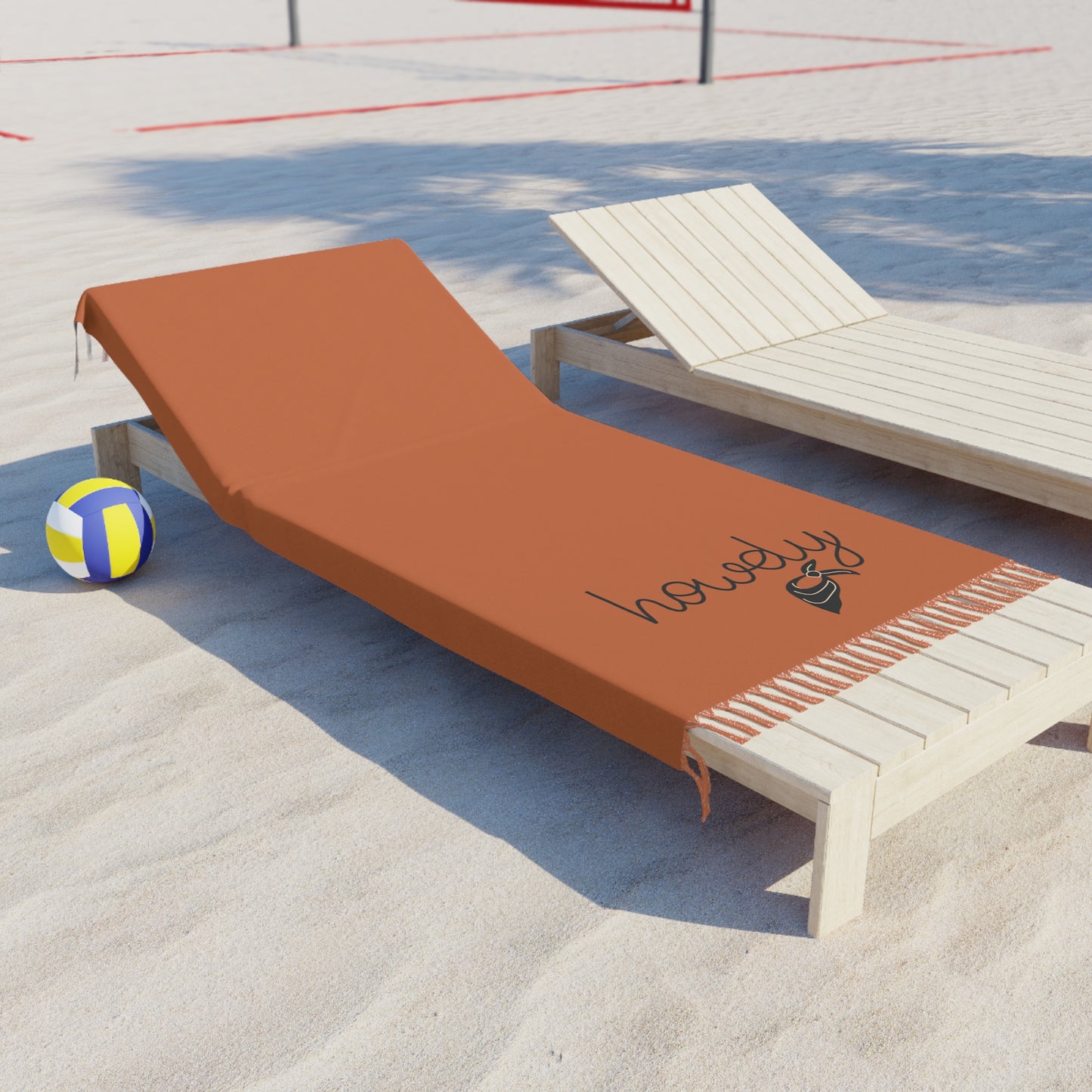 Brown beach towel with 'howdy' logo on a wooden lounge chair by a poolside.