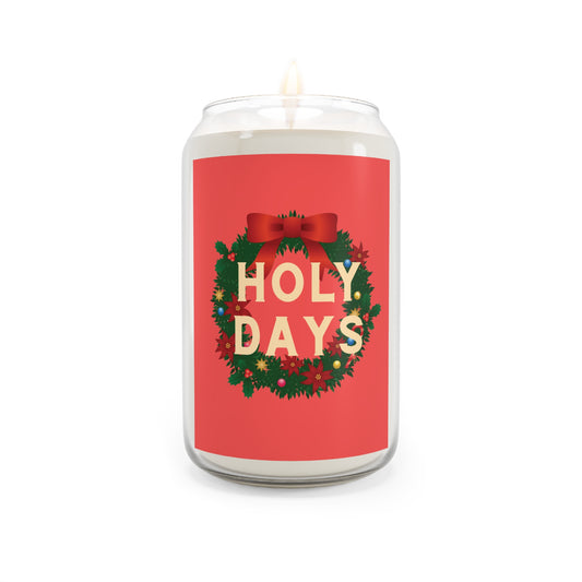 A white wax candle in a clear glass jar with a red label that reads 'HOLY DAYS' in cream letters, surrounded by a green wreath with red bow and holiday details, on a white background.