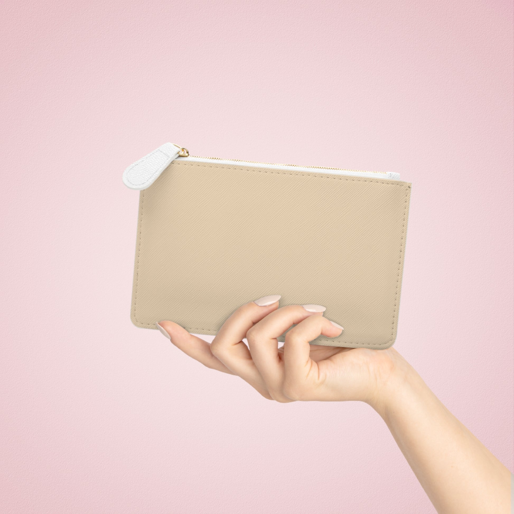 Beige pouch with a white zipper held by a hand against a pink background