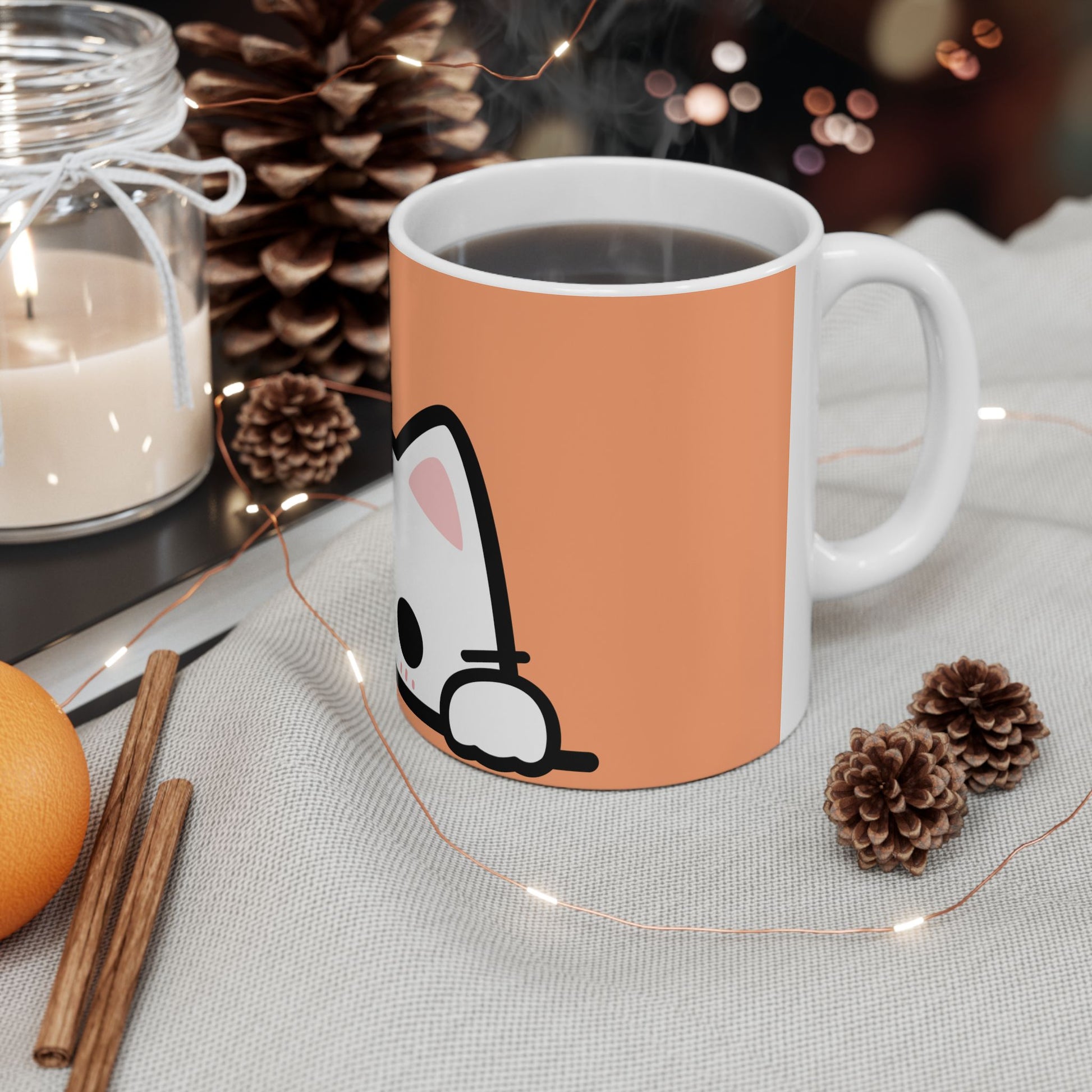Mug with a cartoon design on an autumn-themed table with candles and pinecones.