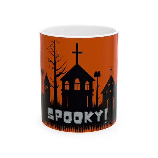 A white ceramic mug featuring a Halloween-themed graphic print with black silhouettes of spooky houses, a bare tree, and the word 'SPOOKY!' in bold white letters against an orange background.