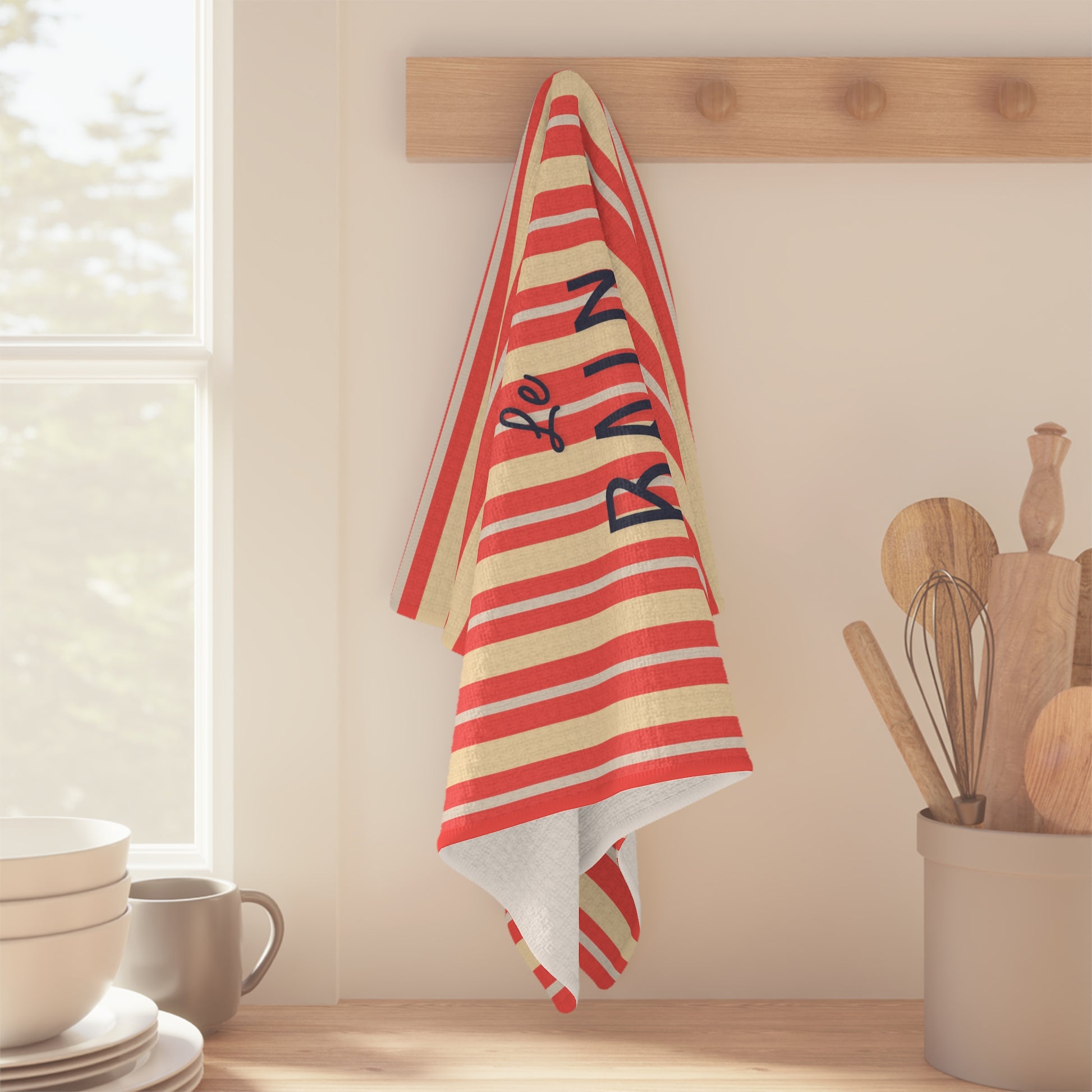 Red and white striped towel with 'Le Rain' text hanging on a wooden rack in a kitchen.