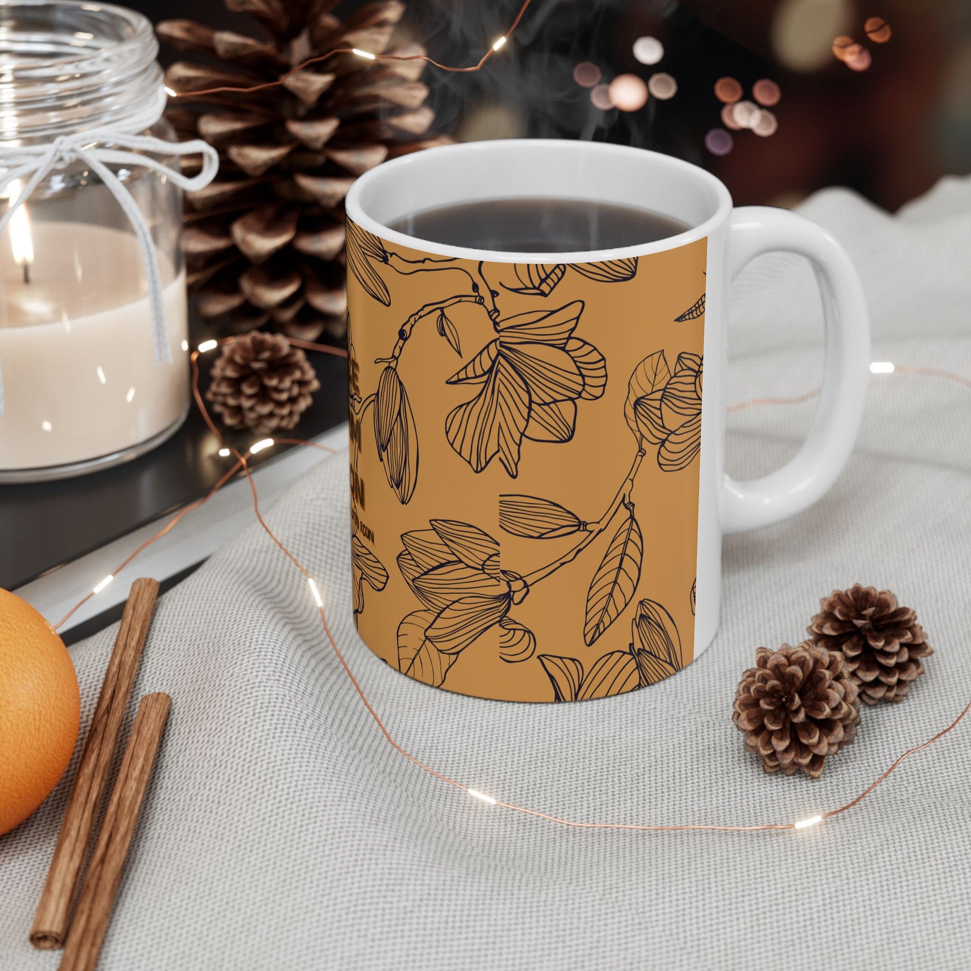 Mug with floral pattern on a table with candles, oranges, and pinecones.