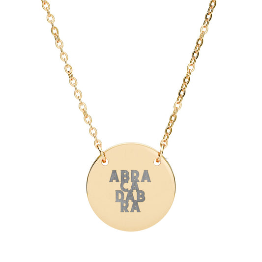 Gold necklace with a round pendant featuring 'ABRACADABRA' on a white background