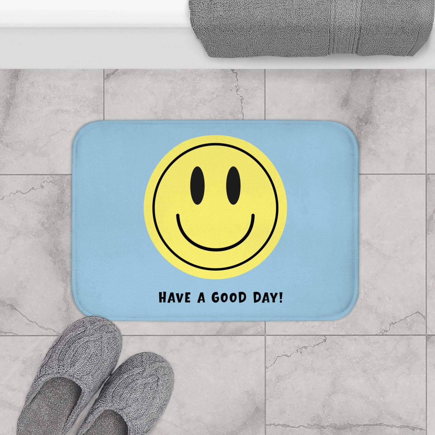 Light blue bath mat with yellow smiley face and 'Have a Good Day!' text on a marble floor.