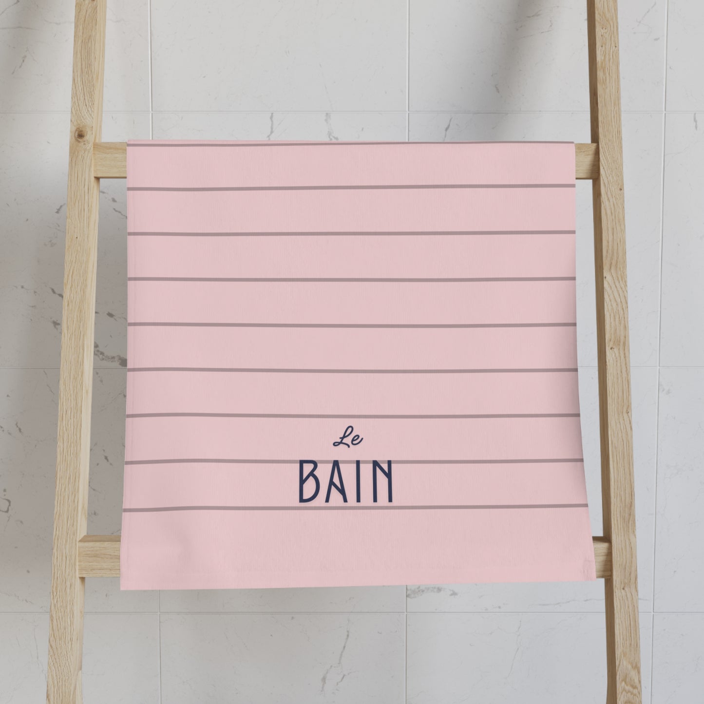 Pink towel with 'Le Bain' text on a wooden ladder against a white wall.