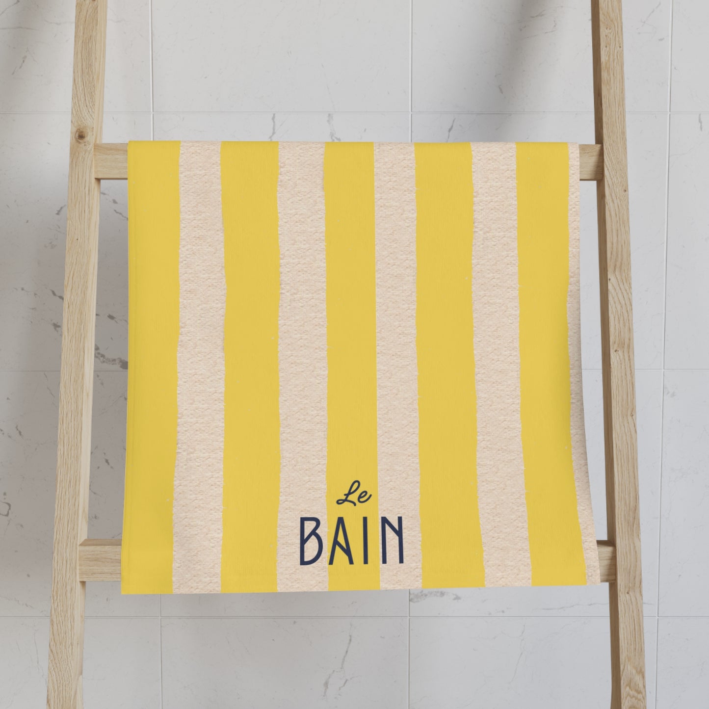 Yellow and beige striped towel with 'Le Bain' text on a wooden ladder against a white wall.