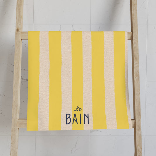 Yellow and beige striped towel with 'Le Bain' text on a wooden ladder against a white wall.