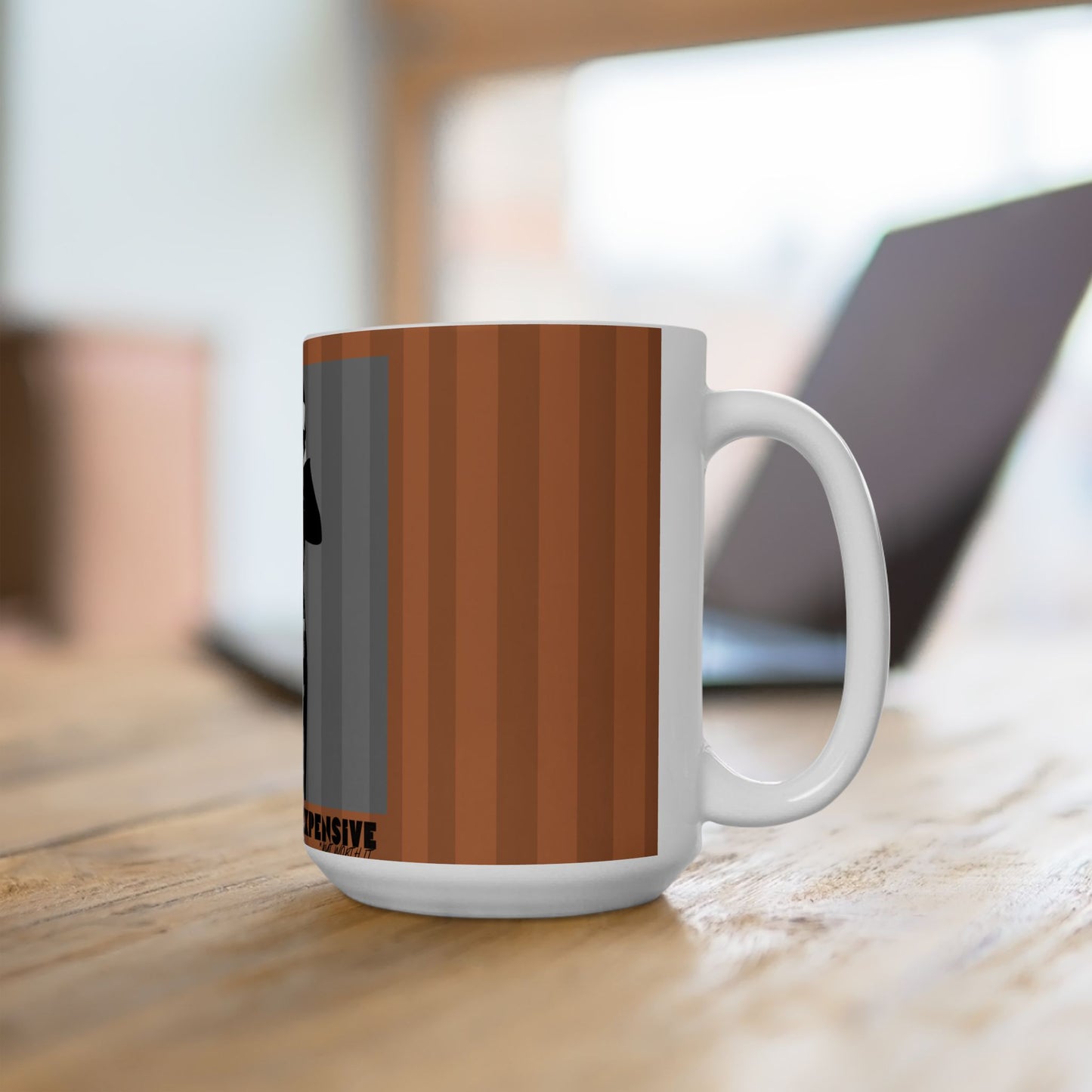 A white ceramic mug with a brown and gray striped design, sitting on a wooden table with a blurred laptop in the background.