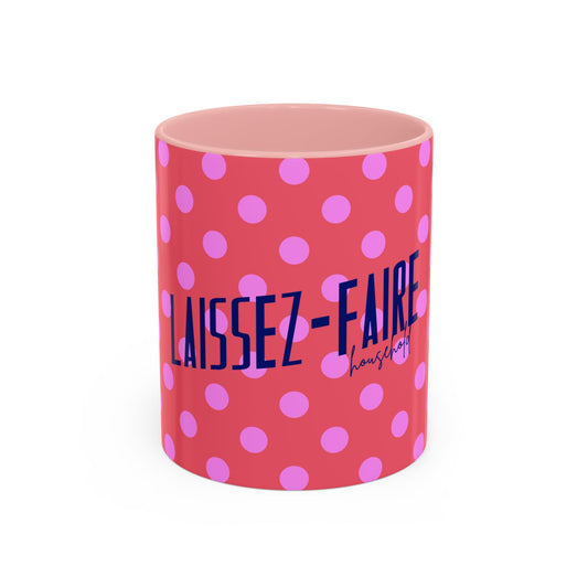 A pink ceramic mug with a pink and purple polka dot pattern and the text 'LAISSEZ-FAIRE housing' printed on the front, set against a plain white background.