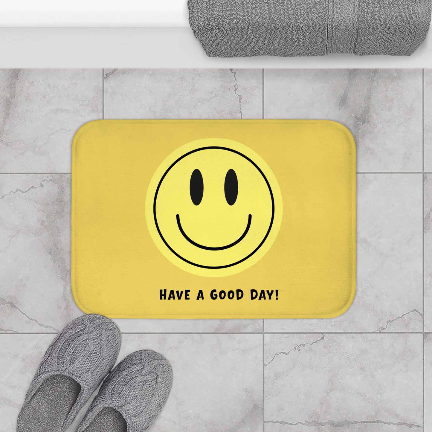 Yellow bath mat with smiley face and 'Have a Good Day!' text on a marble floor.