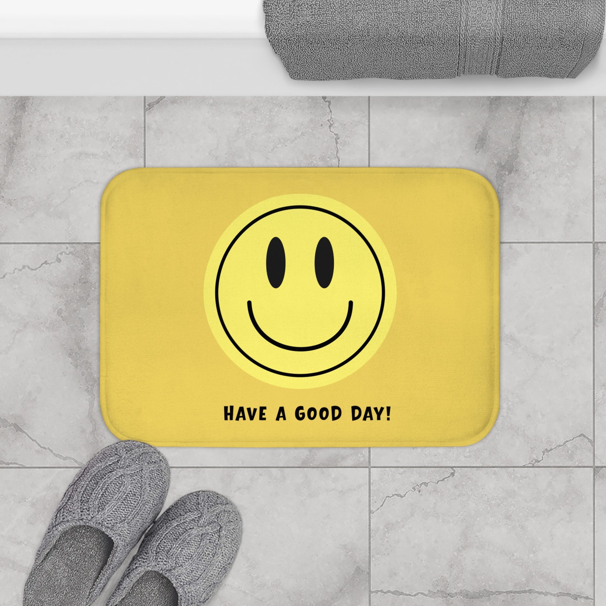 Yellow bath mat with smiley face and 'Have a Good Day!' text on a marble floor.