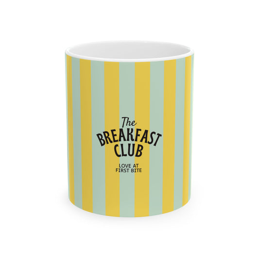 A white ceramic mug featuring vertical stripes in yellow and light mint green, with black text reading 'The Breakfast Club' and 'LOVE AT FIRST BITE'.