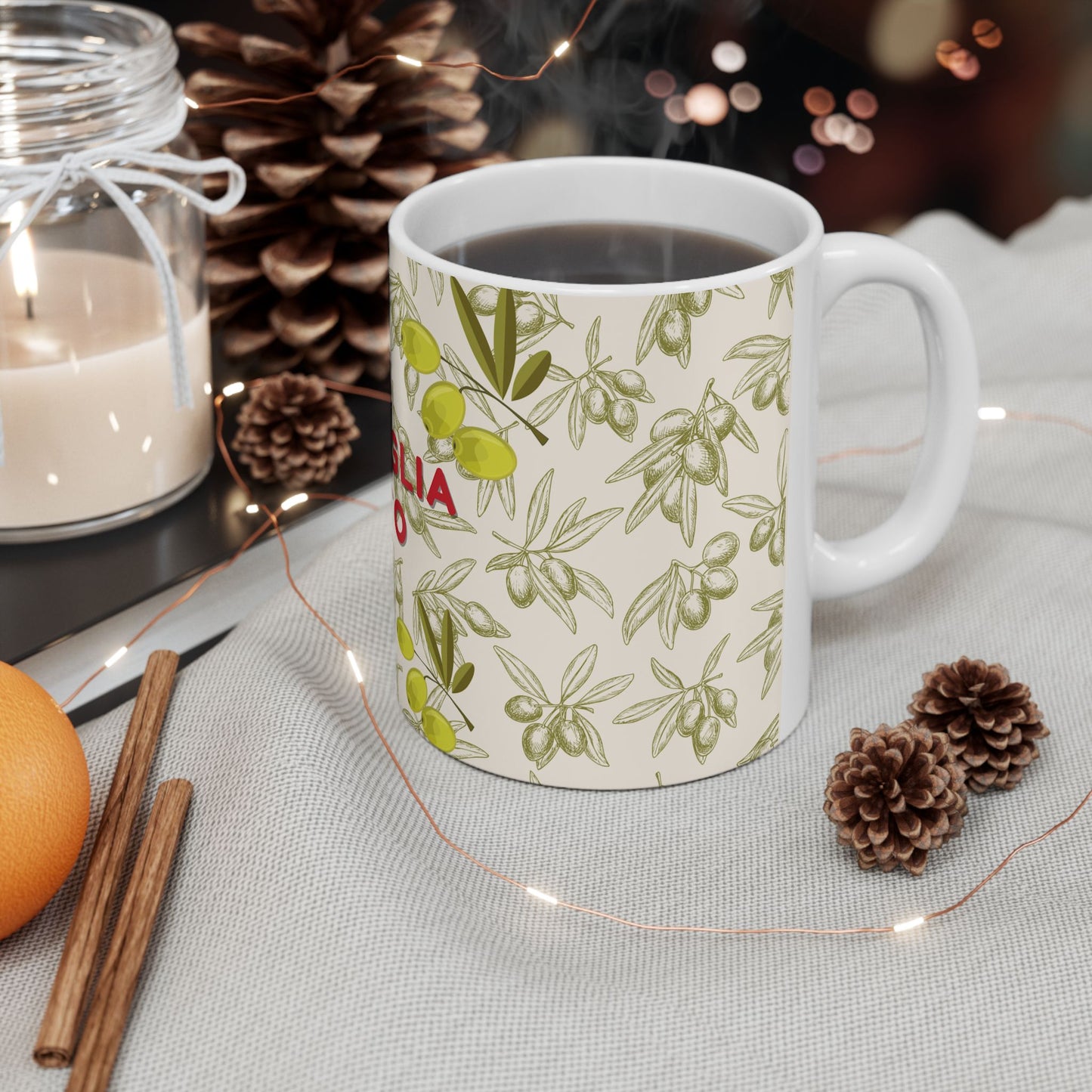 Mug with olive pattern on a table with candles, oranges, and pinecones.