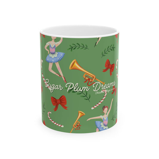 A white ceramic mug with a green holiday-themed print featuring ballerina dancers, red bows, candy canes, and gold trumpets, with the text 'Sugar Plum Dreams' and 'Christmas' on a white background.