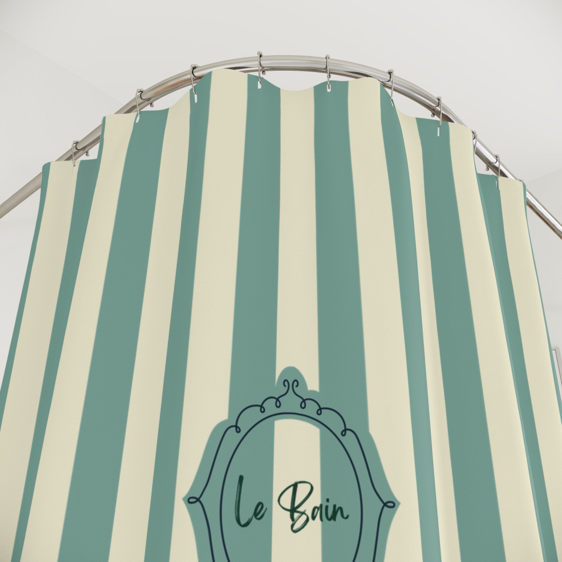 A shower curtain with vertical mint green and cream stripes, featuring a decorative black frame graphic with the text 'Le Bain' in script. The curtain is hung from a curved silver metal rod against a plain light gray wall.