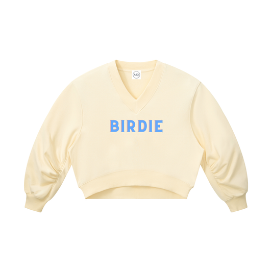 A pale yellow V-neck long-sleeve crop sweatshirt with 'BIRDIE' printed in blue block letters across the chest, displayed on a solid white background.