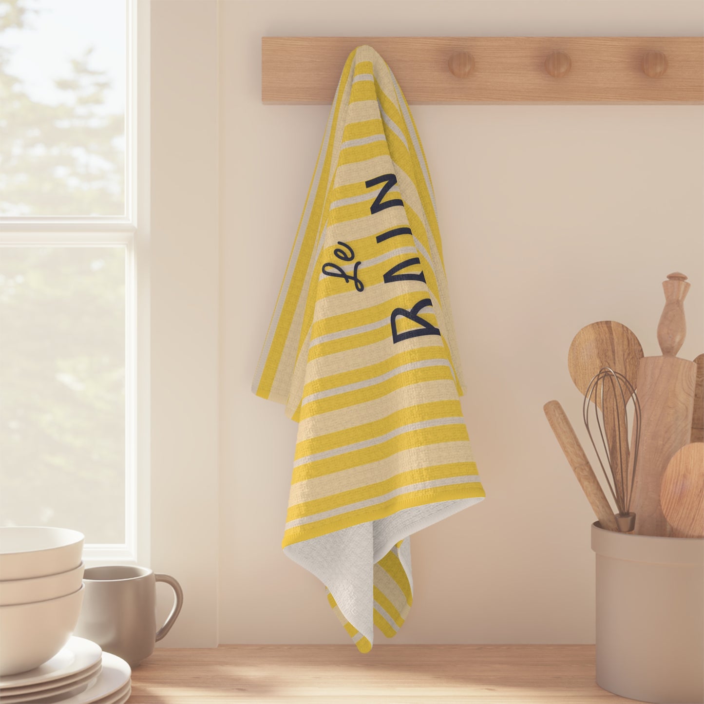 Yellow and white striped towel with 'Le Bain' text hanging on a wooden rack in a kitchen.