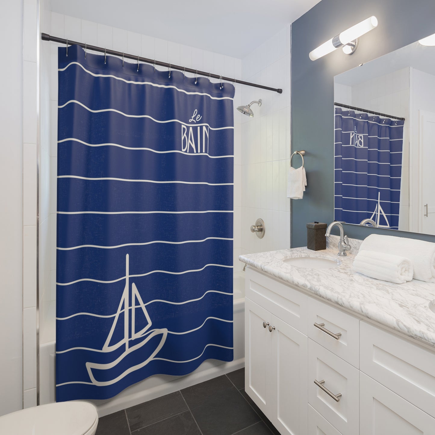 Bathroom with a blue shower curtain featuring a sailboat design, white cabinets, and a mirror.
