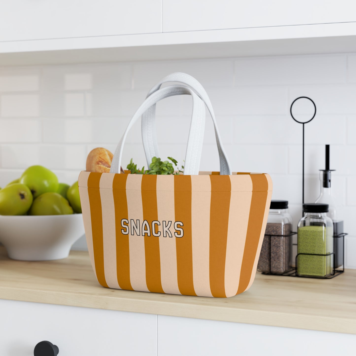 Striped snack bag labeled 'SNACKS' on a kitchen counter with fruits and kitchen items in the background.