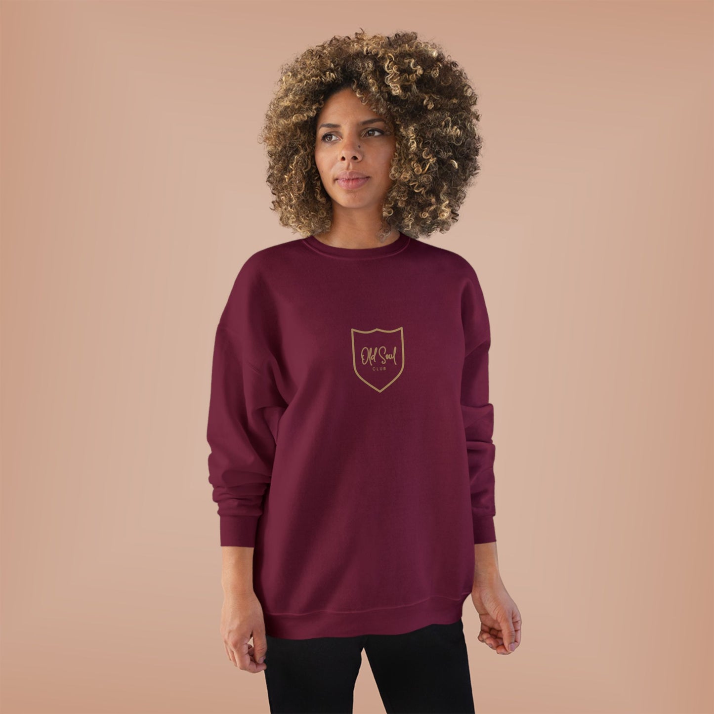 Woman wearing a burgundy sweatshirt with an Old Soul Club logo on a beige background