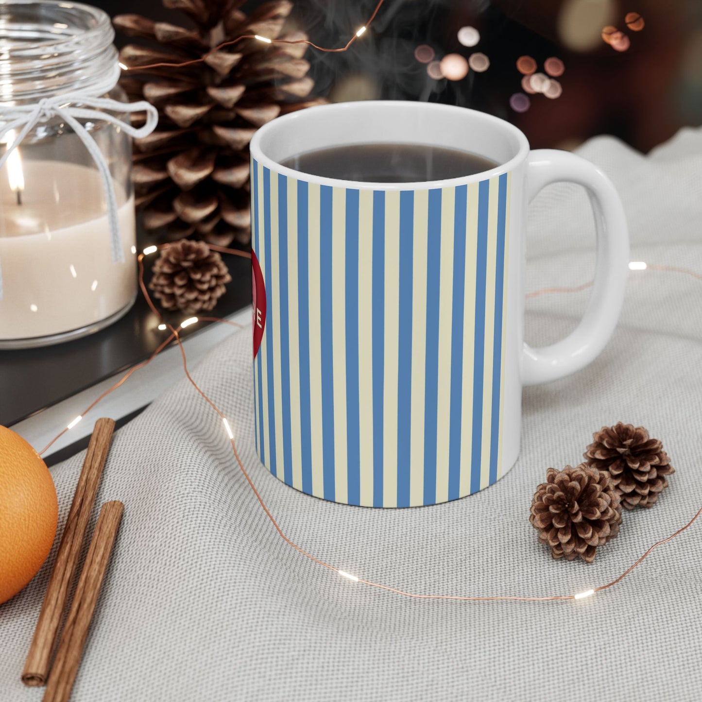 Striped mug with a small orange, cinnamon stick, and pine cones on a table.