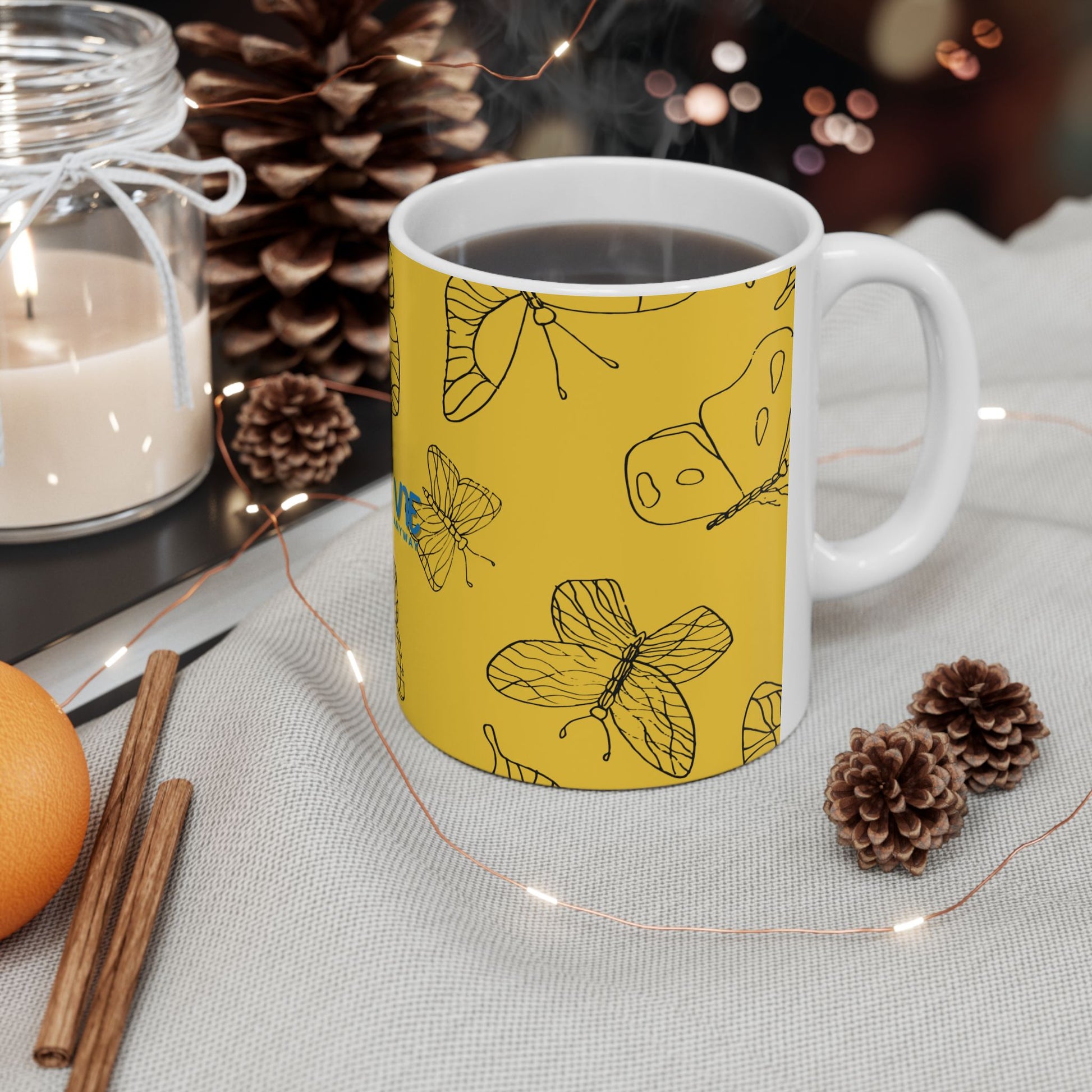 Yellow mug with butterfly design on a table with candles and pinecones
