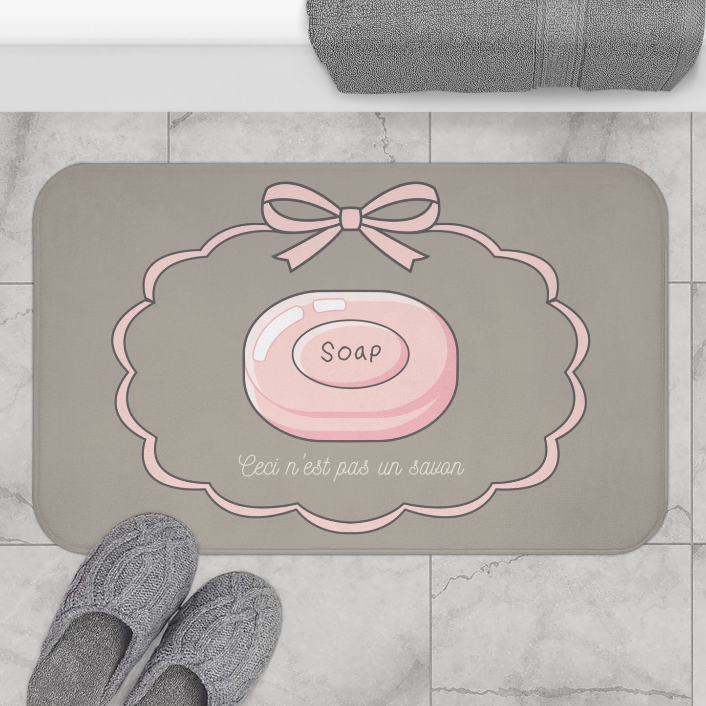 Gray bath mat with pink soap design and text on a marble floor.