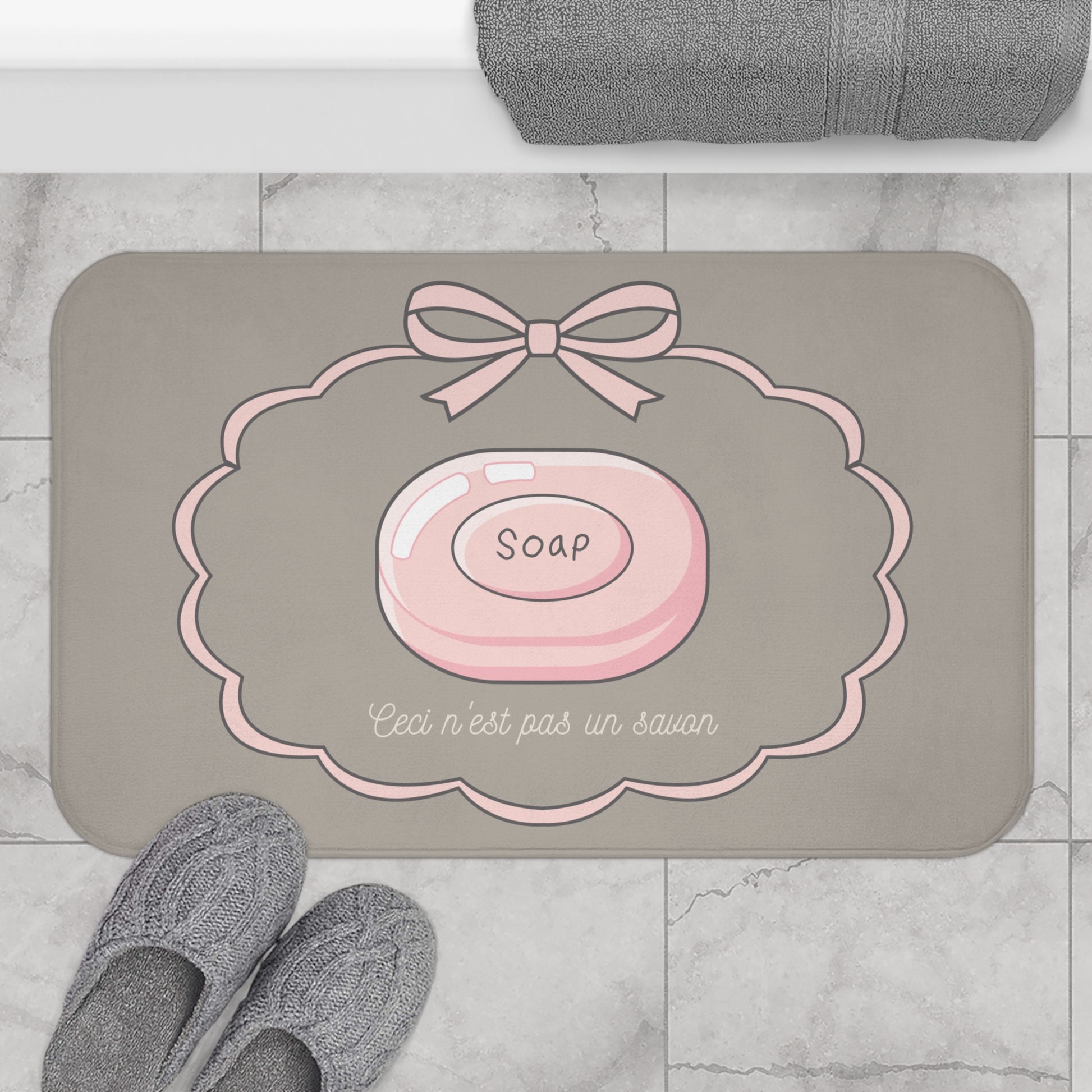 Gray bath mat with pink soap design and text on a marble floor.