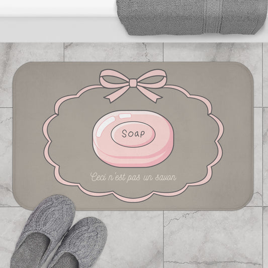 Gray bath mat with pink soap design and text on a marble floor.