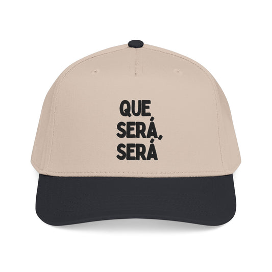 A beige and black baseball cap with the text 'QUE SERÁ, SERÁ' printed in black on the front panel, shown against a plain white background.