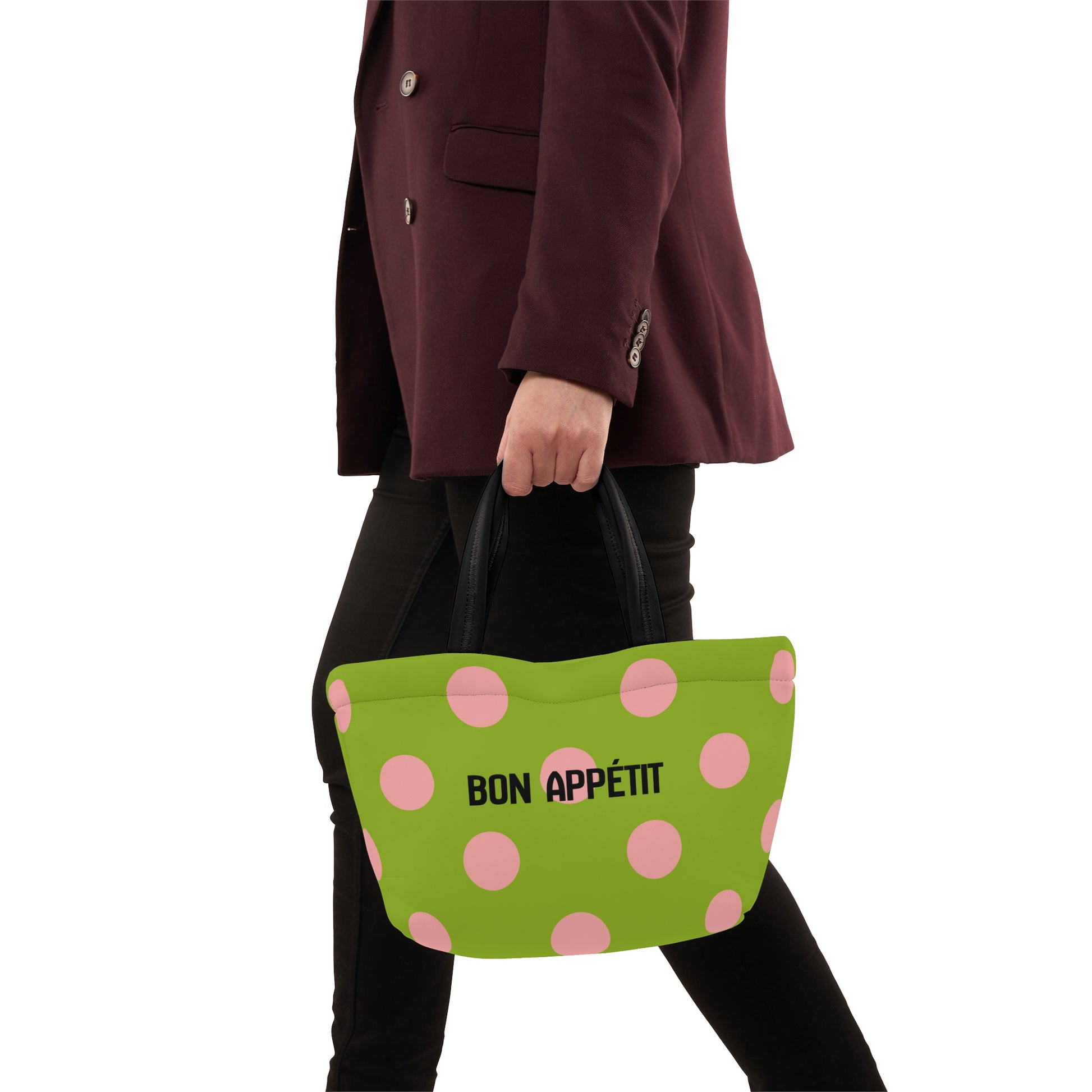 Person holding a green bag with pink polka dots and 'Bon Appetit' text.