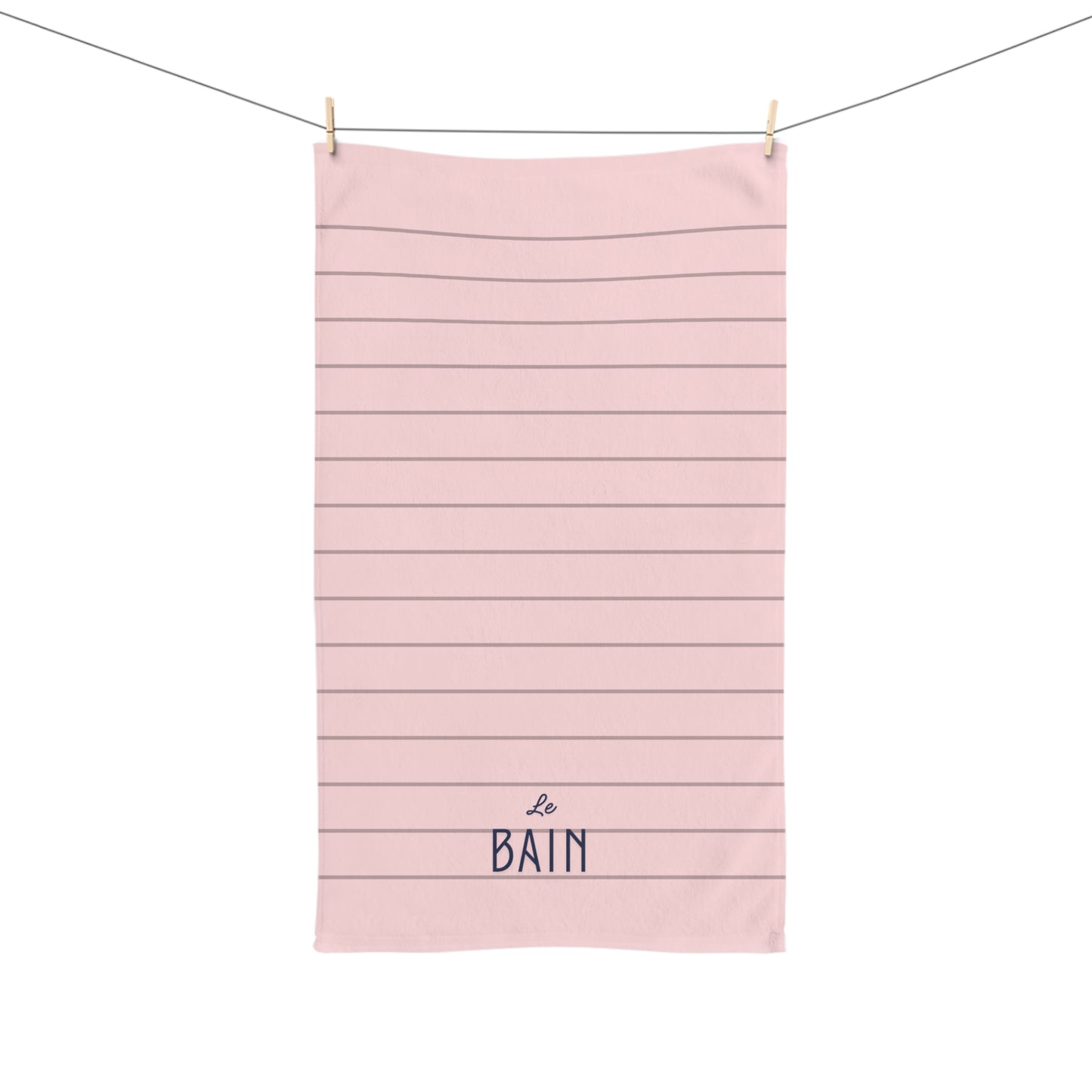Pink towel with horizontal stripes and 'Le Bain' text hanging on a line.