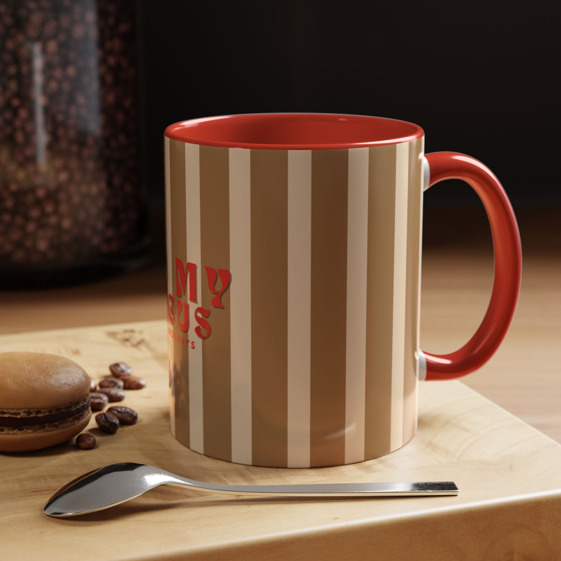 Striped mug with red interior and handle, surrounded by coffee beans and a spoon on a wooden surface.