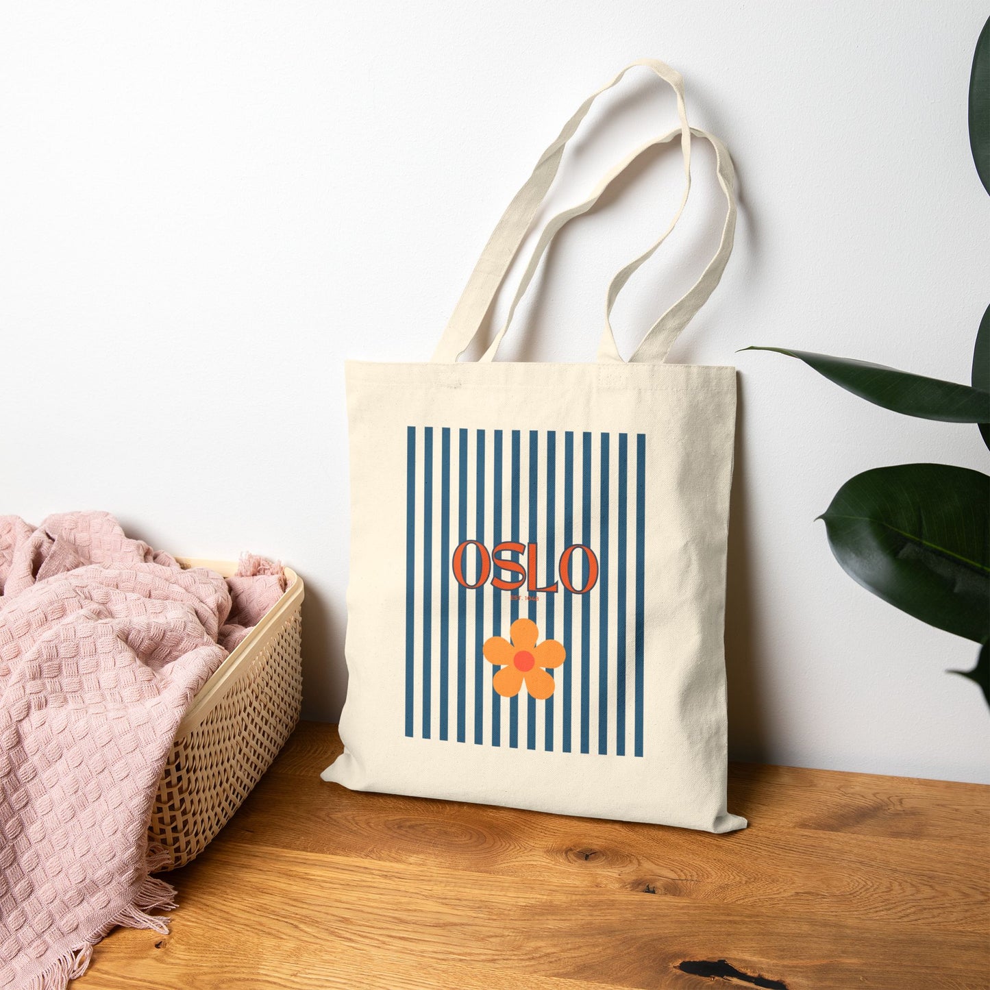 Tote bag with 'OSLO' and a flower design on a wooden surface with a white wall background.