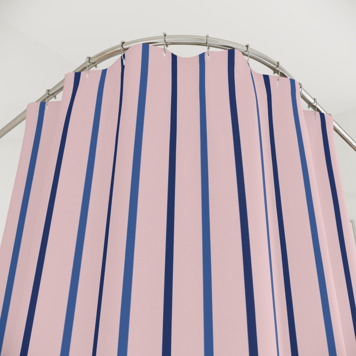 Pink shower curtain with vertical navy blue stripes hanging from silver rings on a curved metal rod.