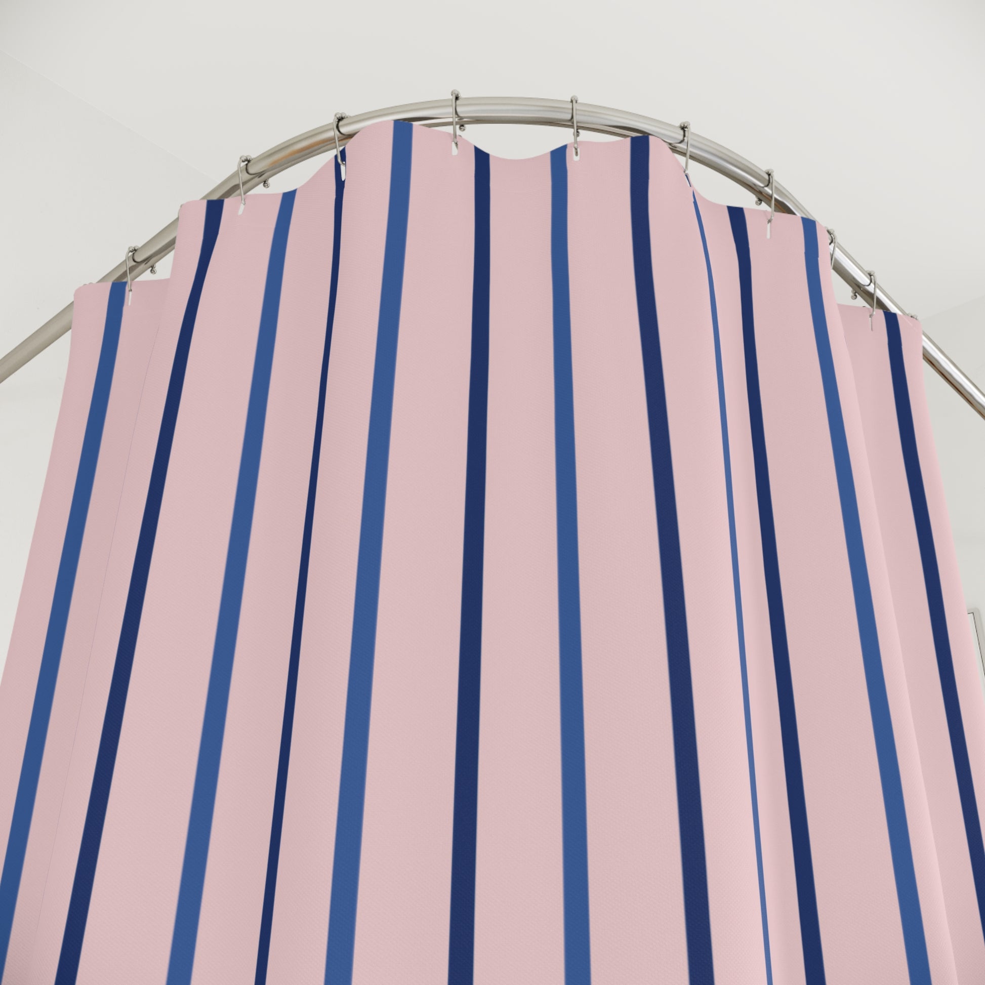 Pink shower curtain with vertical navy blue stripes hanging from silver rings on a curved metal rod.