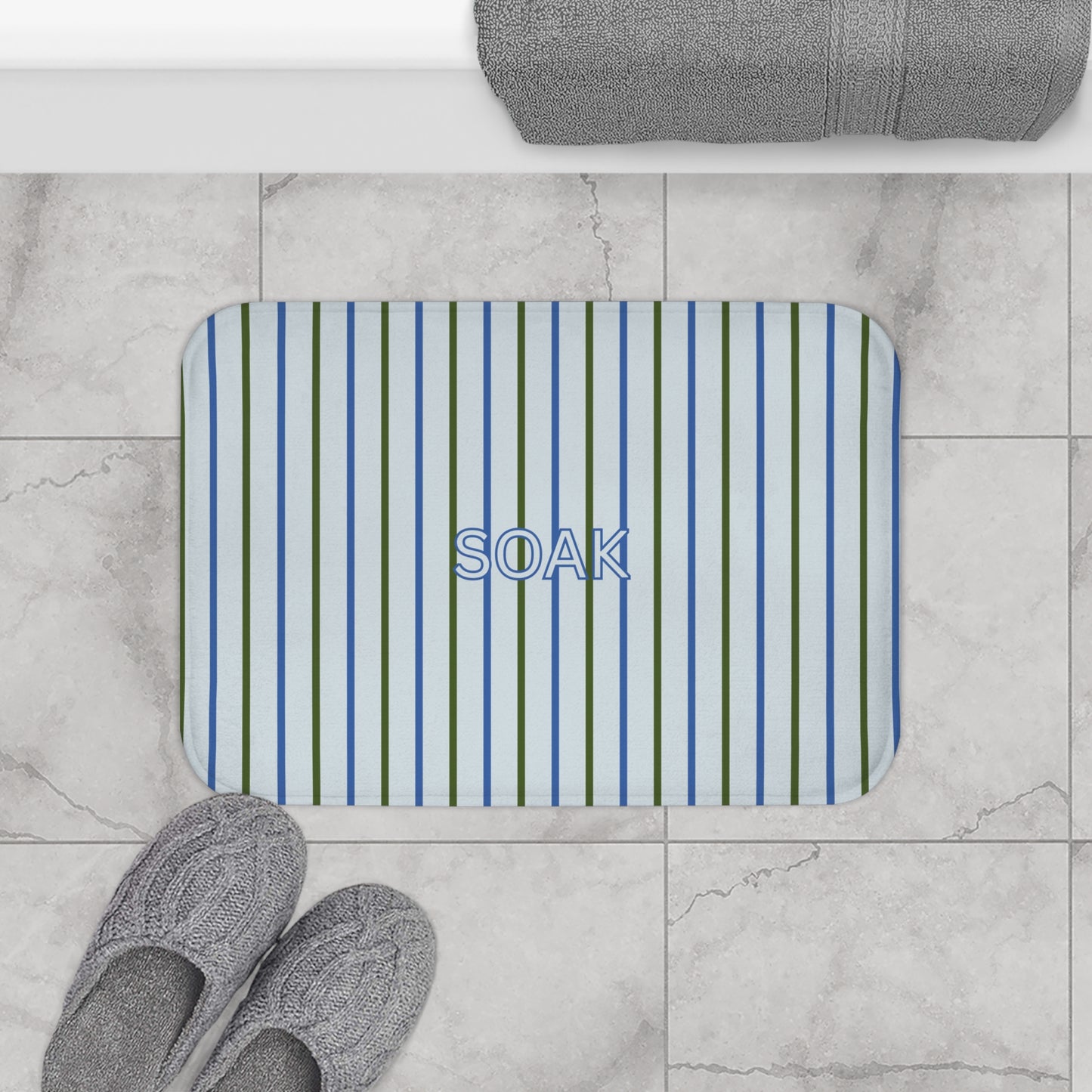 Striped bath mat with 'SOAK' text on a marble floor with slippers and a towel.