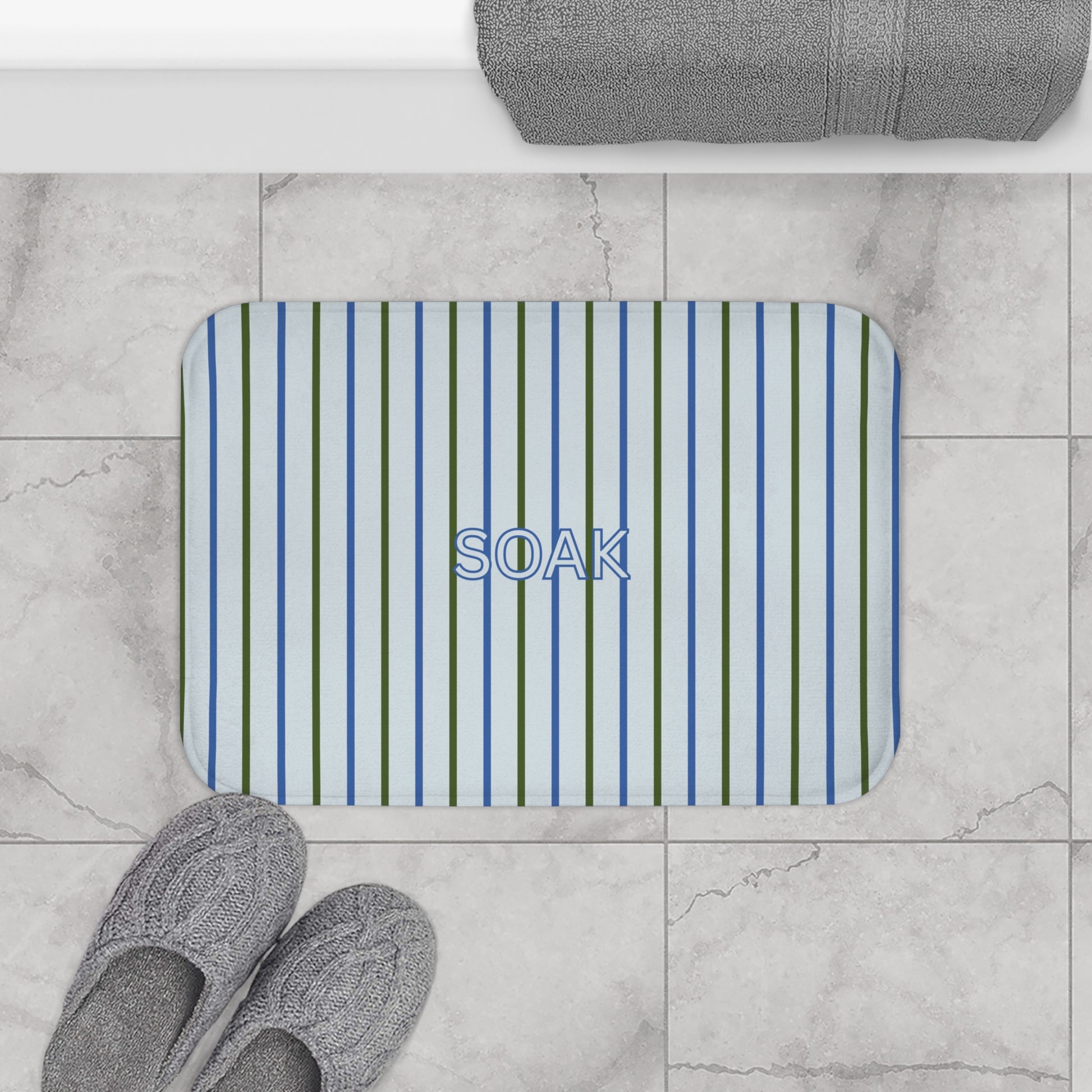 Striped bath mat with 'SOAK' text on a marble floor with slippers and a towel.