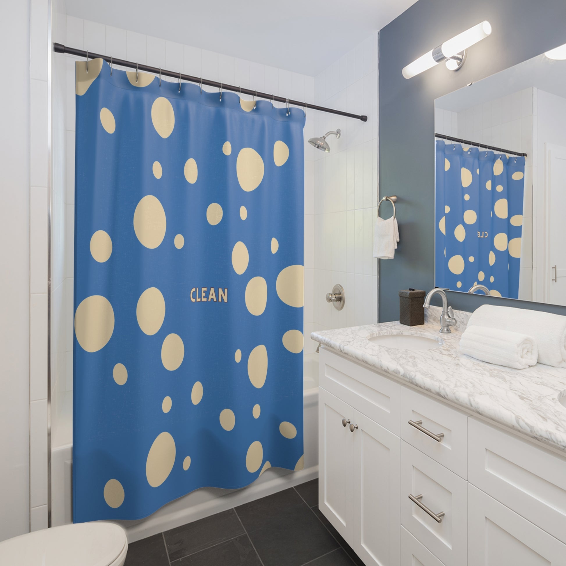 A blue shower curtain with beige polka dots and the word 'CLEAN' printed in the center, shown hanging in a bright white and blue bathroom next to a marble vanity.