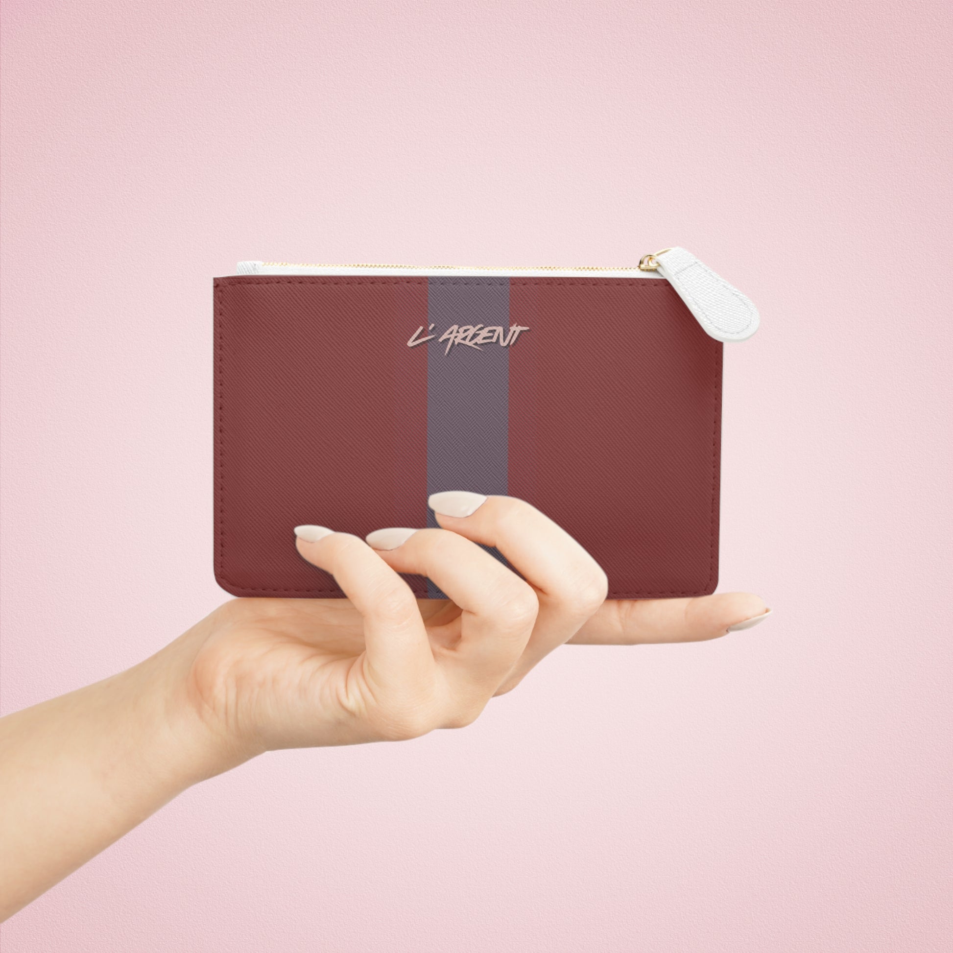 Hand holding a maroon pouch with a gray stripe on a pink background