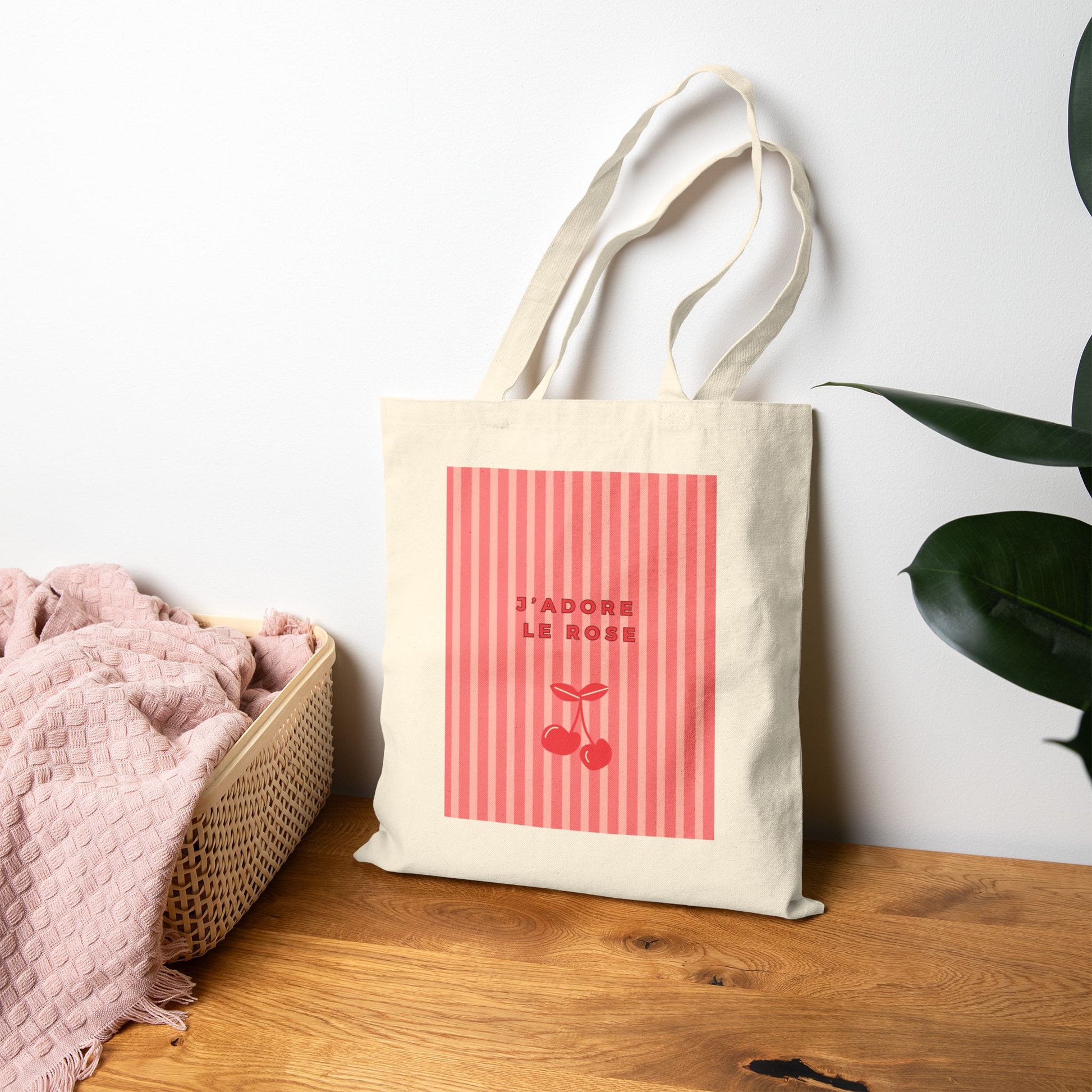 Tote bag with pink design and text on a wooden surface with a white wall background