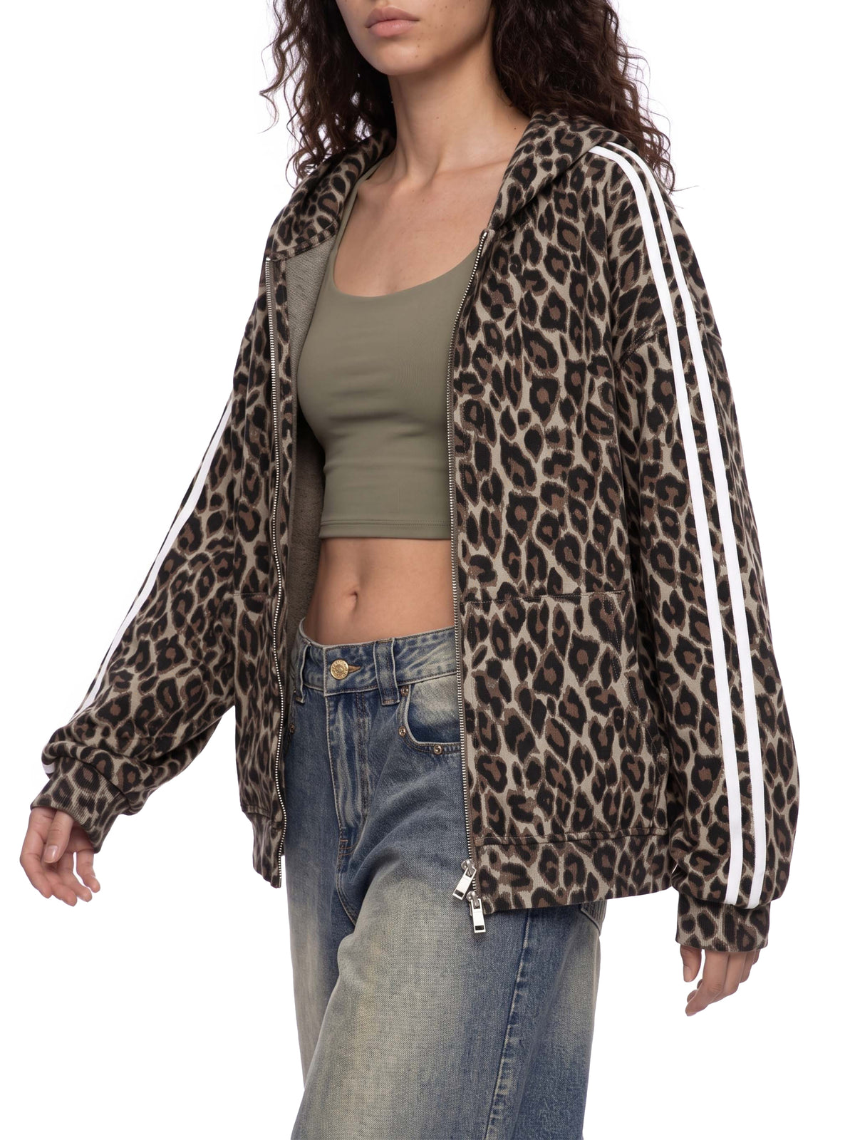 A woman wearing a leopard-print zip-up hoodie with white side stripes, styled over an olive green crop top and blue jeans against a plain white background.