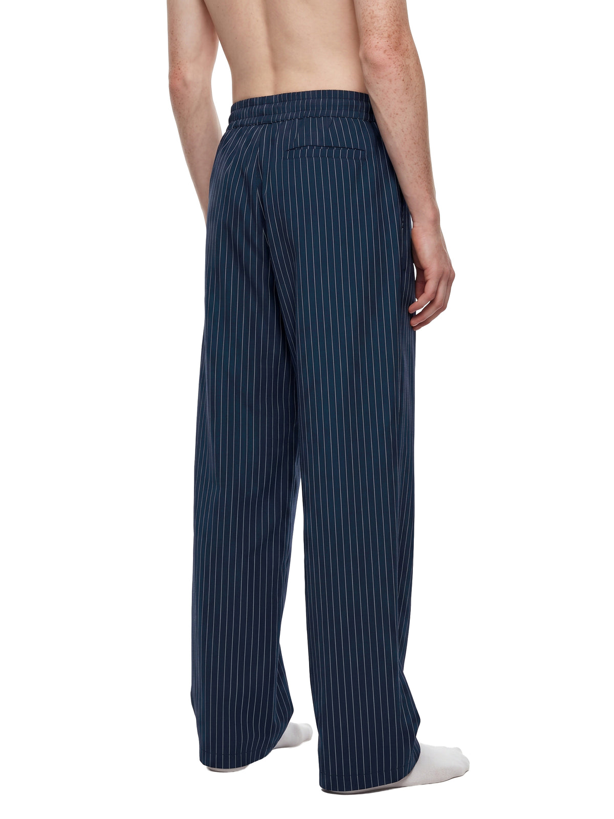 A man shown from the back wearing dark navy pinstriped lounge pants, standing barefoot against a plain white background.