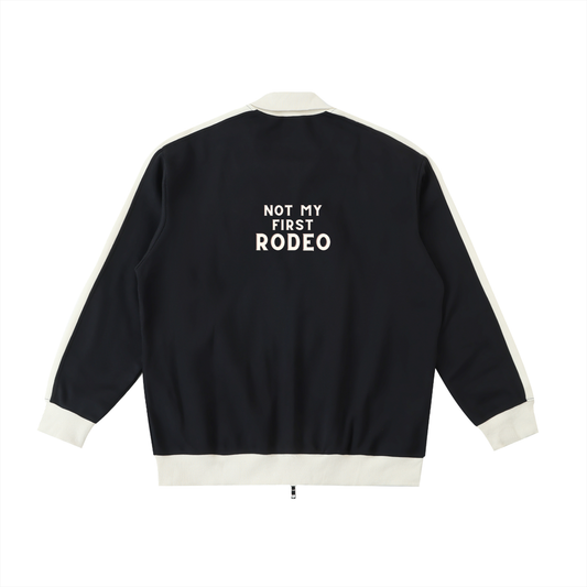 A black bomber jacket with cream ribbed trim and white text on the back reading 'NOT MY FIRST RODEO', shown against a plain white background.
