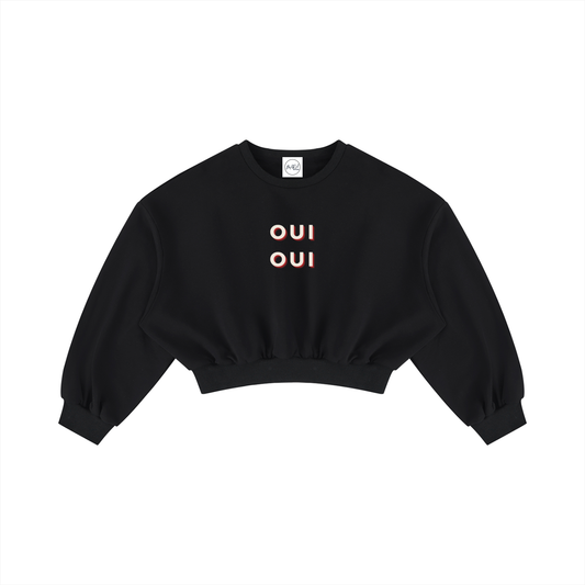 A black cropped crewneck sweatshirt with 'OUI' printed in a peach-pink color on the chest, displayed flat against a solid white background.